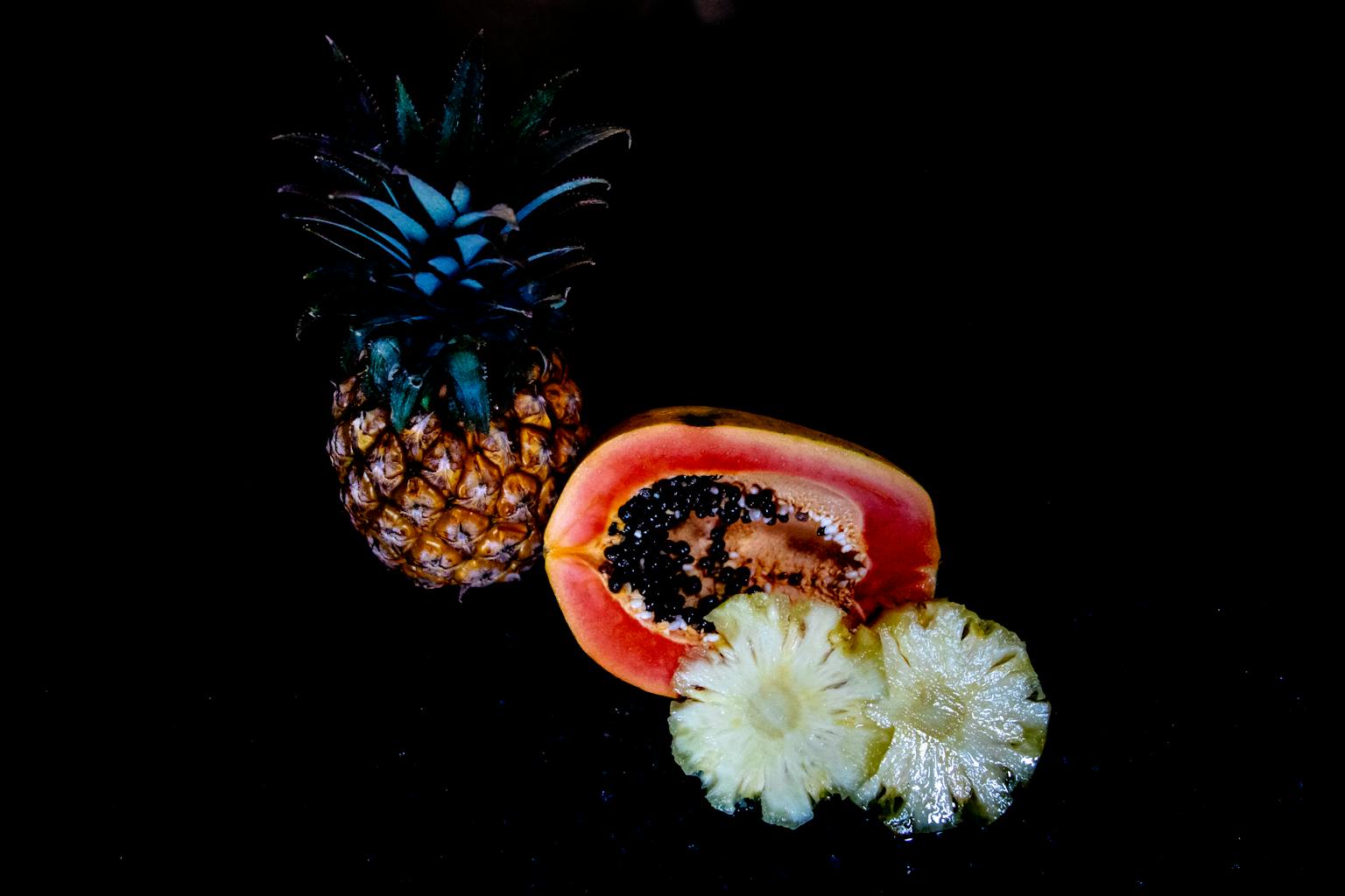 Vibrant display of fresh sliced tropical fruits, including pineapple and papaya, against a dark background.